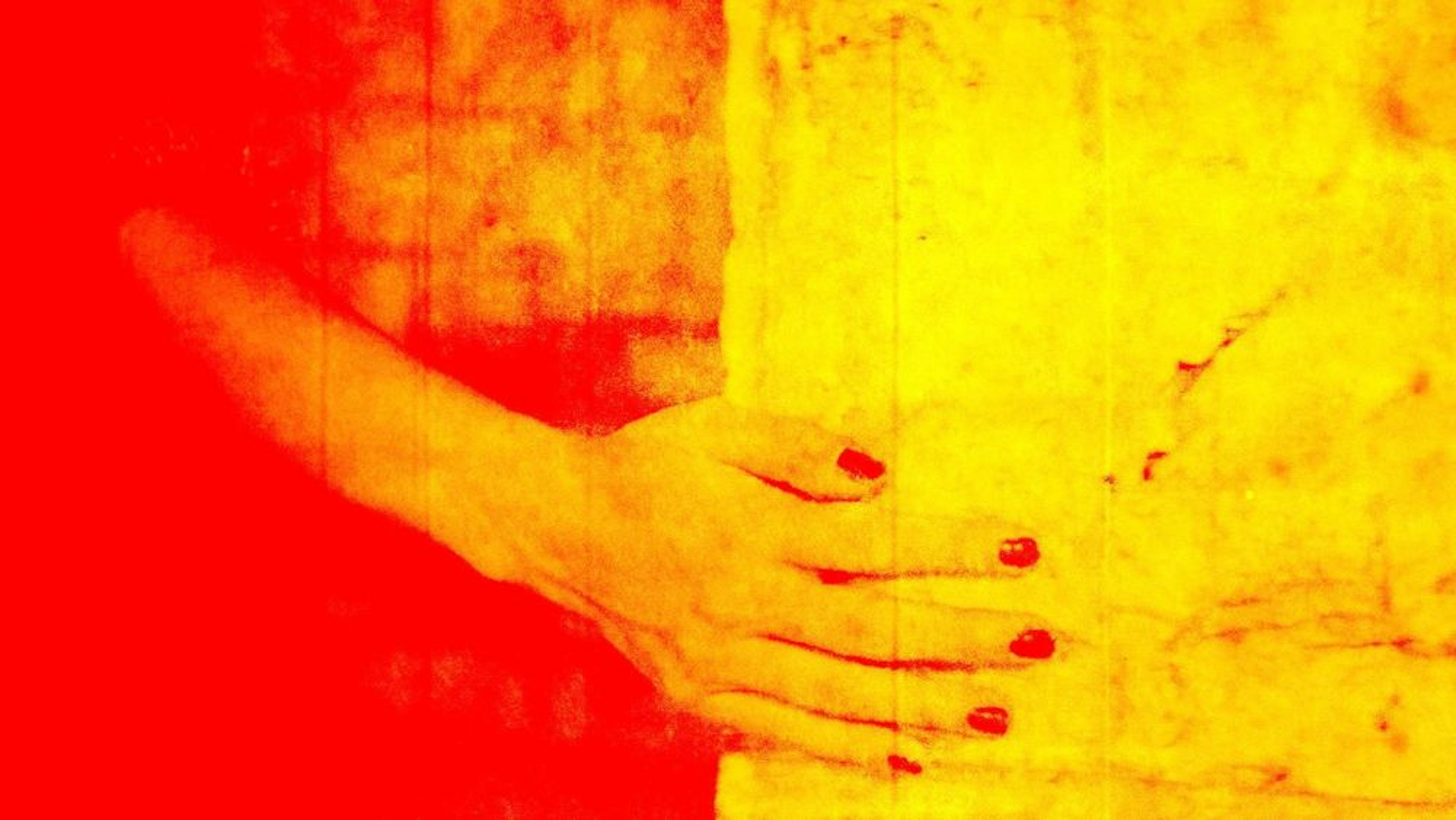 Close-up of a hand with pained nails gently caressing the edge of a wall. The image is tined in saturated red and yellow color.