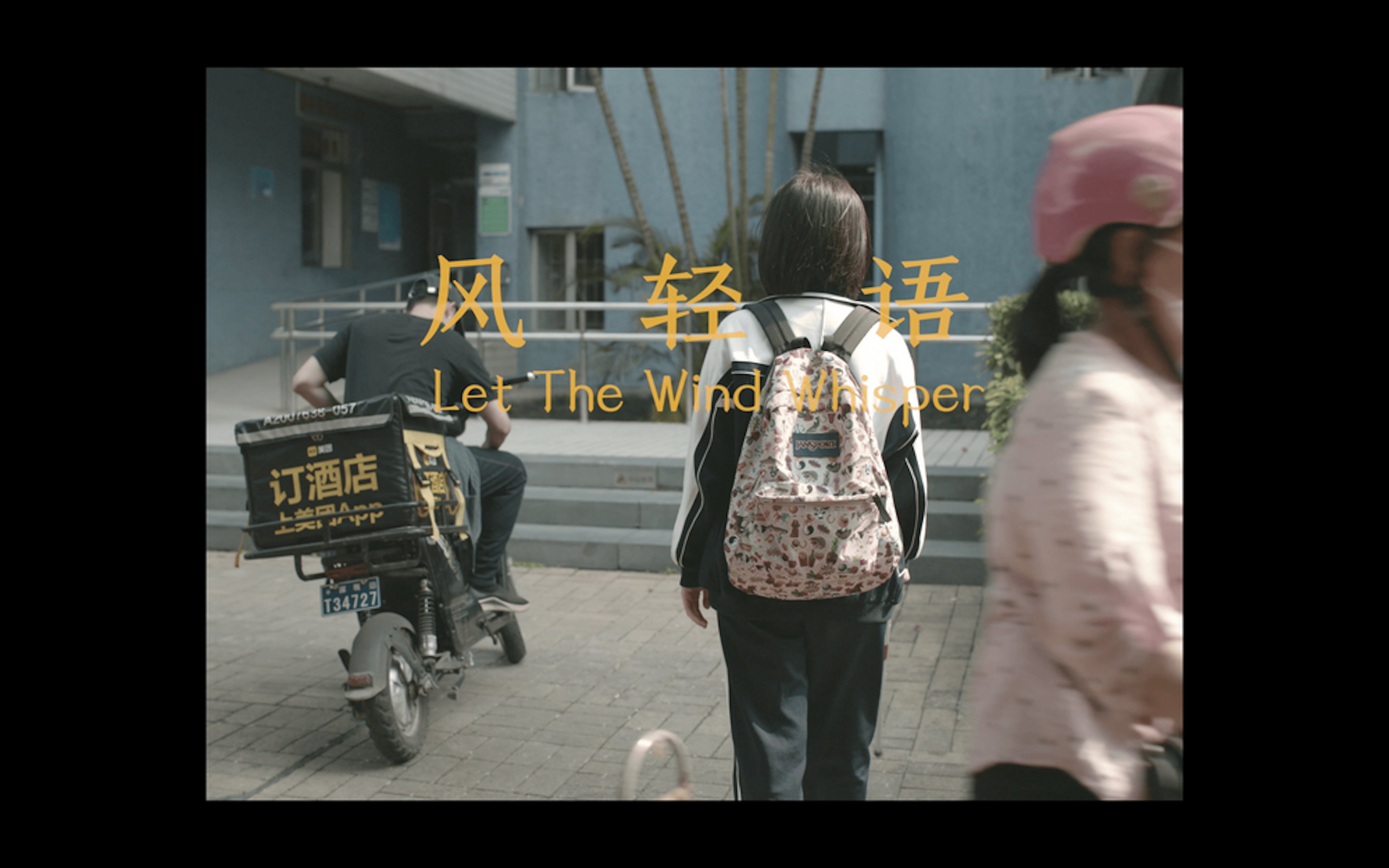 film still showing a child from the back, wearing a backpack and a person on a motorbike beside them. Another child's half body can be seen in the frame. on the image is written: Let The Wind Whisper