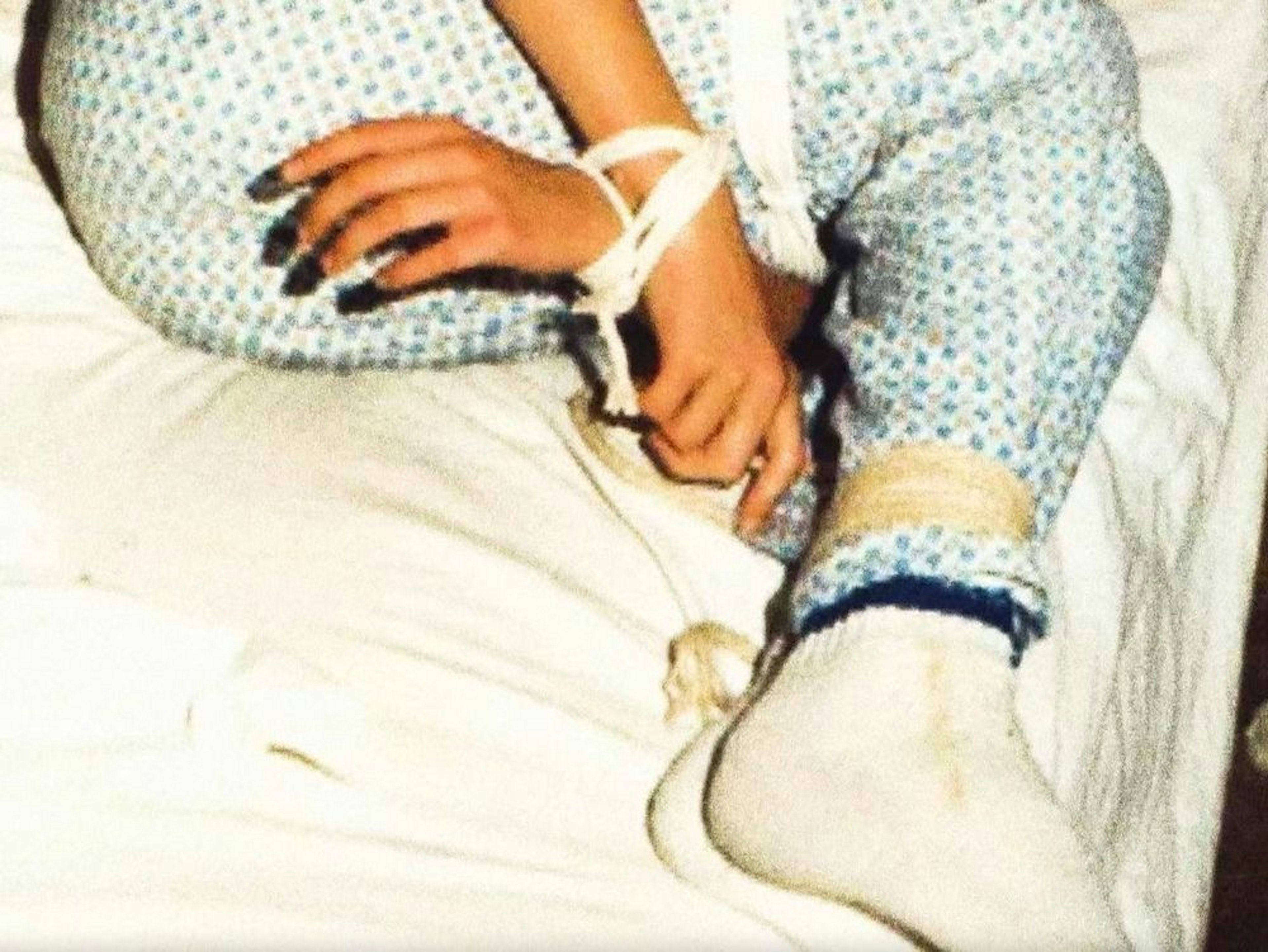 film still showing a person's hands and legs, all tied with rope, while they're lying on a white bedsheet
