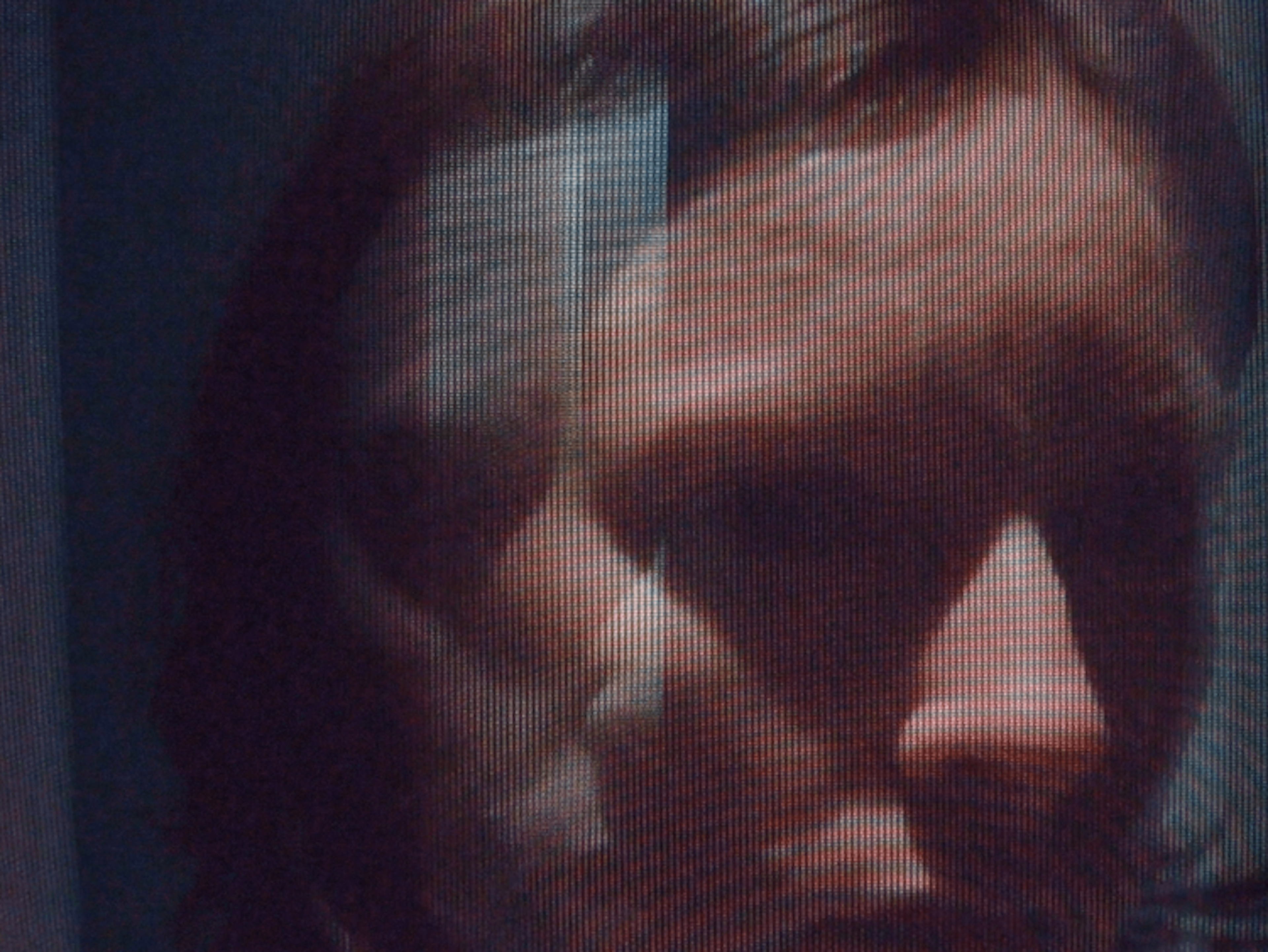 Film still showing a glitchy image of a person's face with harsh light and shadows on their face, on a dark background